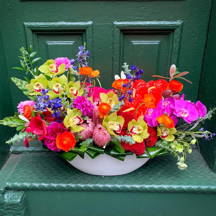 An electric colorful arrangement filled with orchids, delphinium, ranunculus, roses, anthurium, tropical flowers, calla lilly, and more!